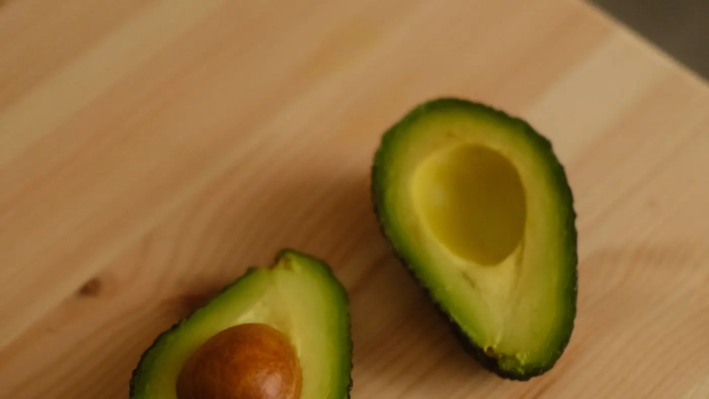 Dos mitades de aguacate, una con la semilla a la vista, sobre una tabla de madera clara