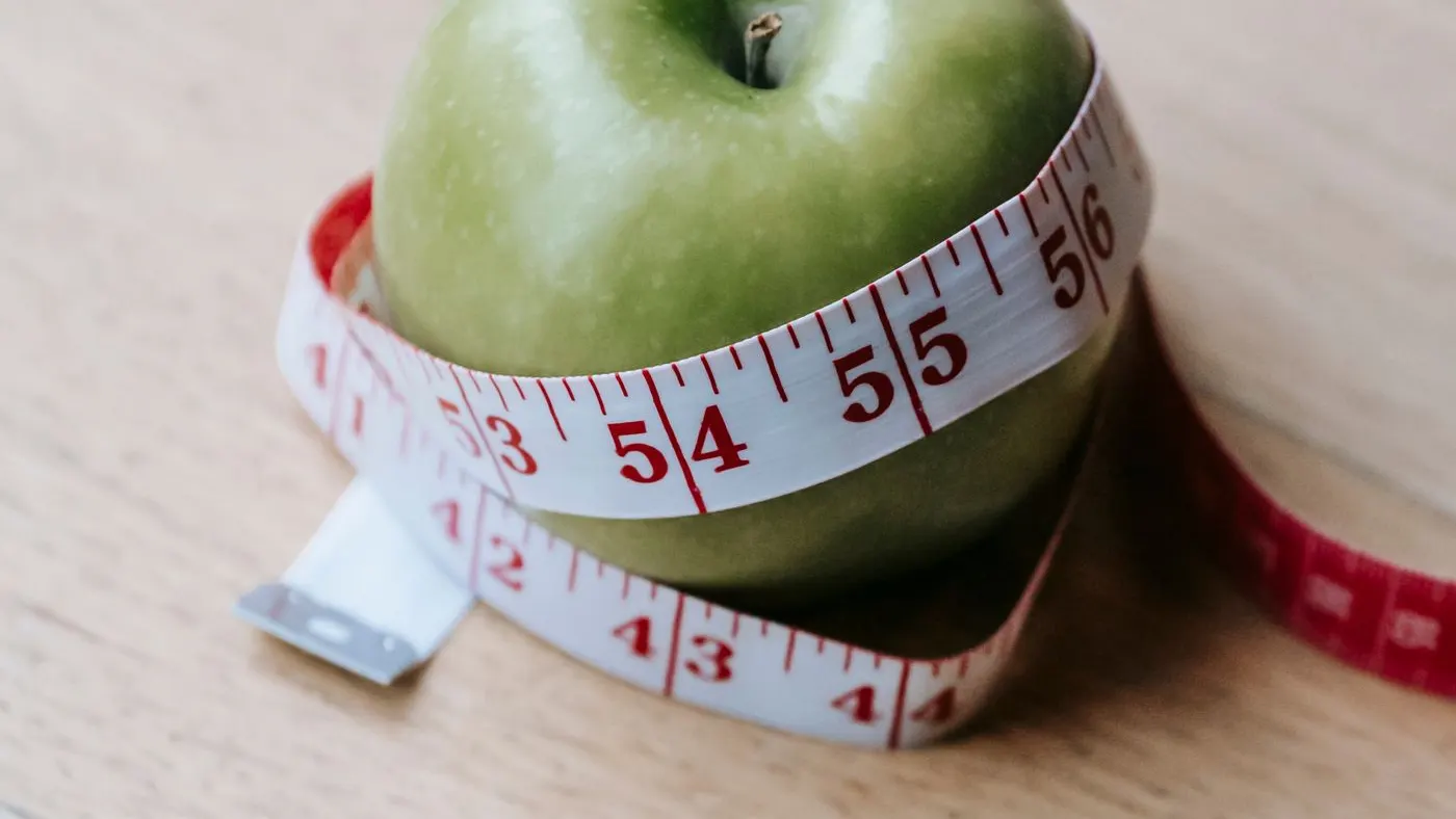 Manzana verde rodeada por una cinta métrica sobre una mesa de madera clara, imagen para hablar de la medida de la cintura