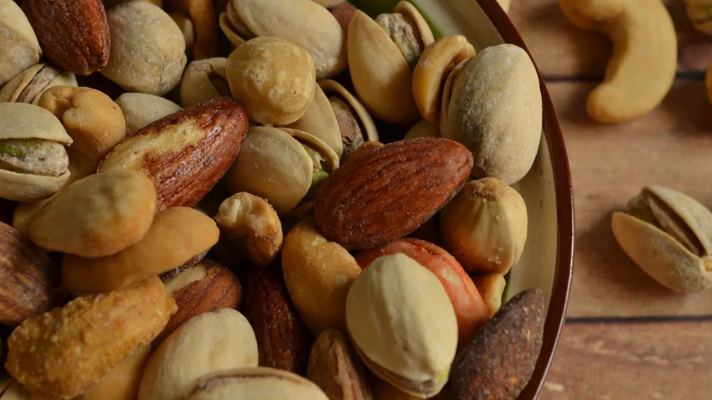 Almendras, pistachos y otros frutos secos en un tazón de cerámica sobre una mesa de madera